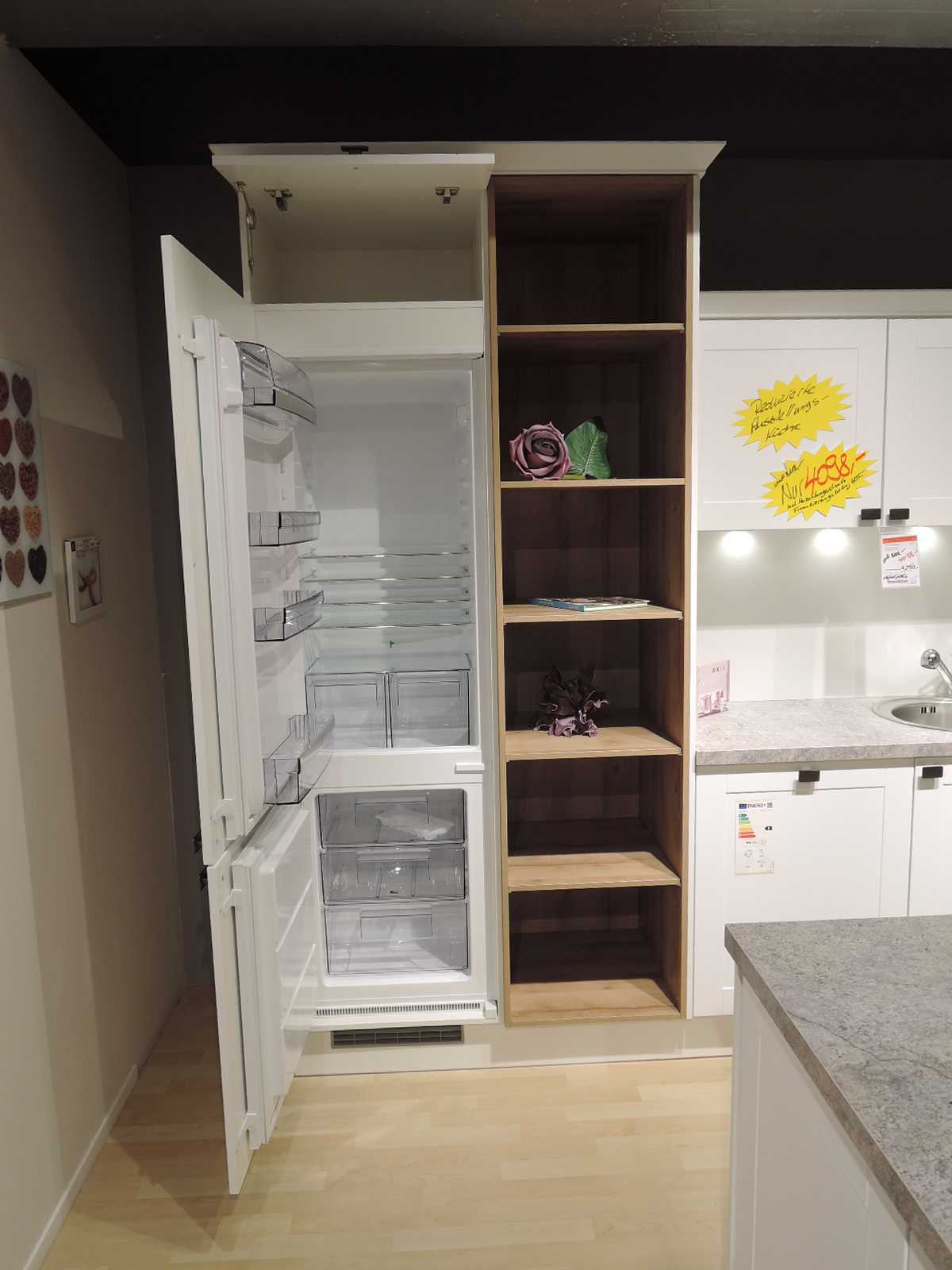 Blick in die geöffnete Kühl-Gefrier-Kombination und auf das offene Regal neben dem Kühlgerät