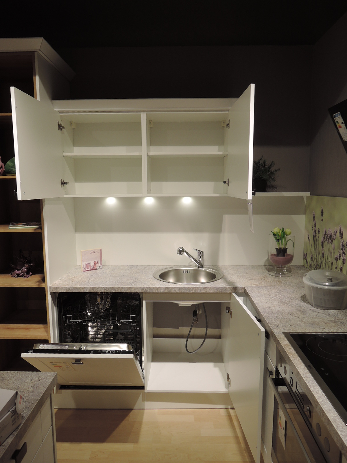 Blick in den geöffneten Geschirrspüler sowie Spülenunterschrank und Hängeschränke über der Spüle