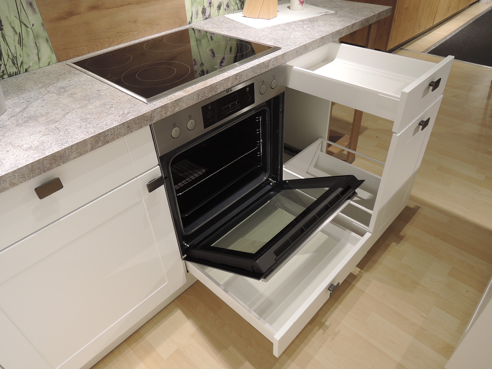 Blick in den geöffneten Herd mit darunterliegender praktischen Schublade für z.B. Backbleche sowie Blick in den Auszug rechts vom Herd