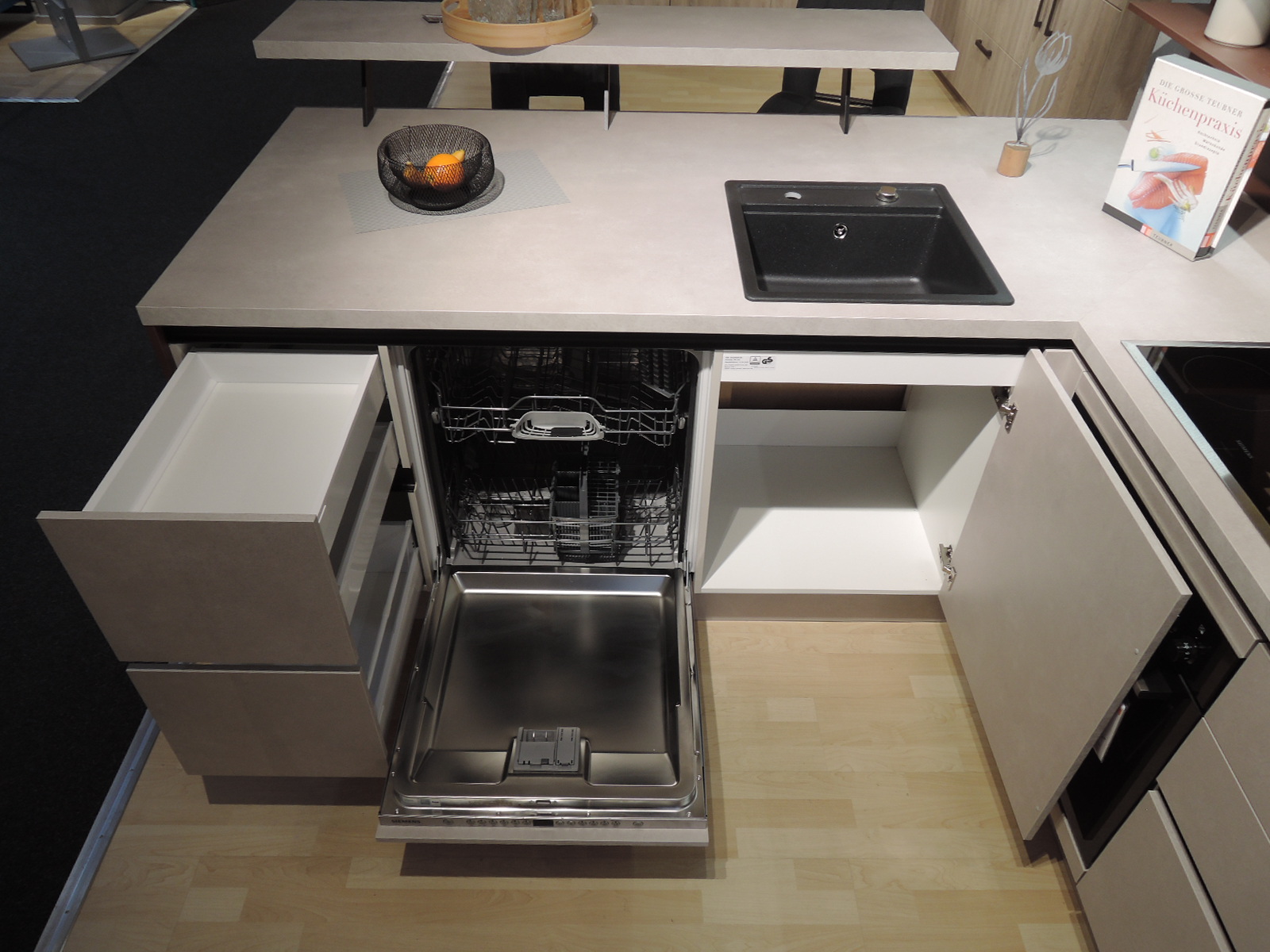 Blick in den geöffneten Geschirrspüler, in den geöffneten Spülenunterschrank rechts vom Geschirrspüler