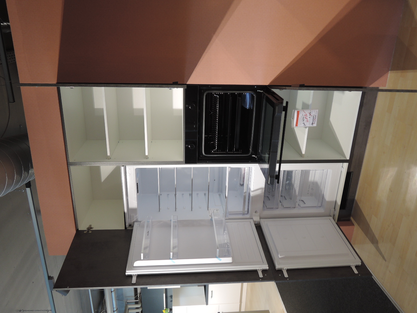 Blick in die geöffnete Kühl-Gefrier-Kombination und links davon in den in die Wand eingelassenen geöffneten Geräteschrank in dem sich auch der Backofen befindet